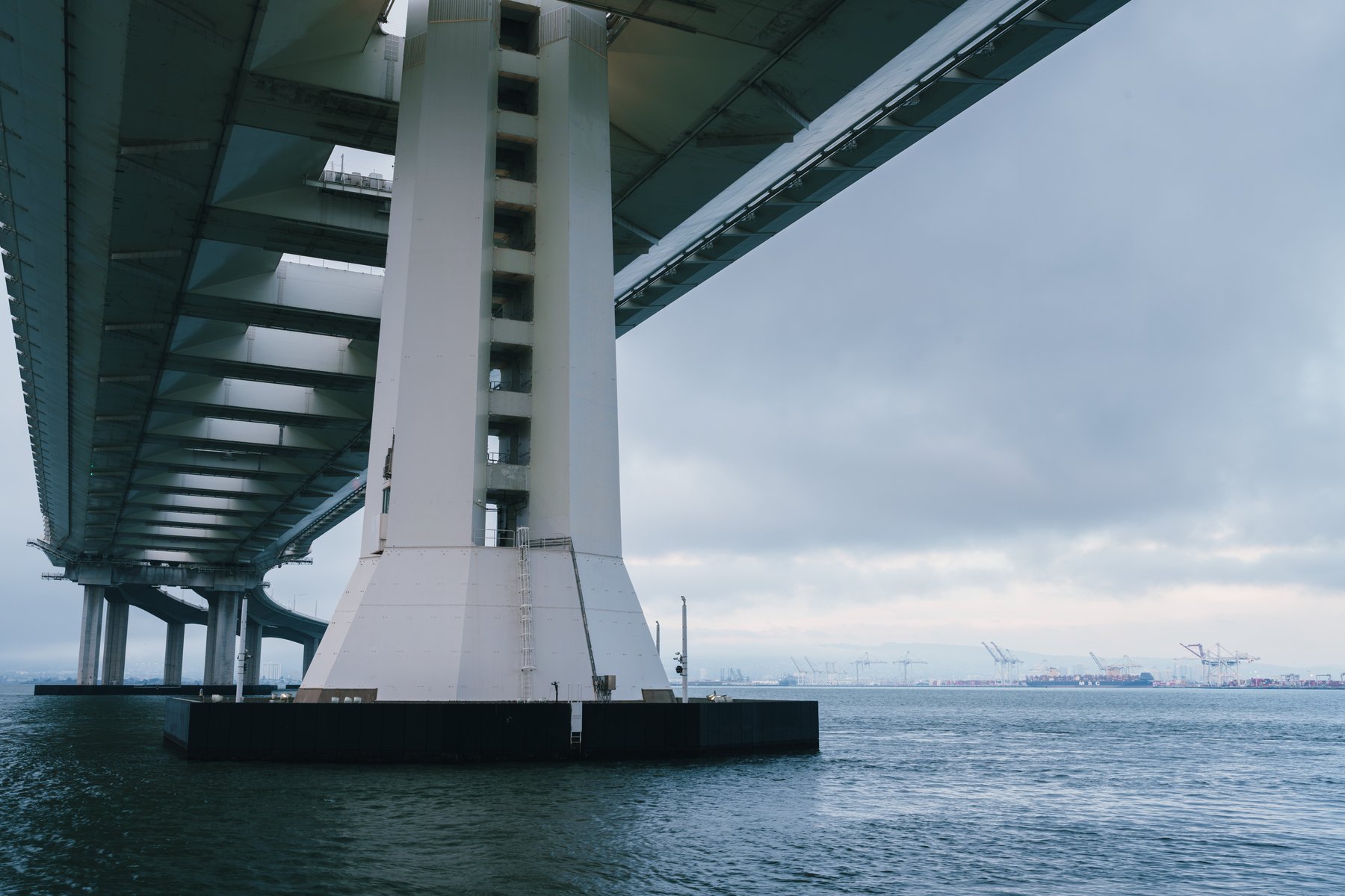 A bridge tower with shipping cranes and a cargo ship visible across the water