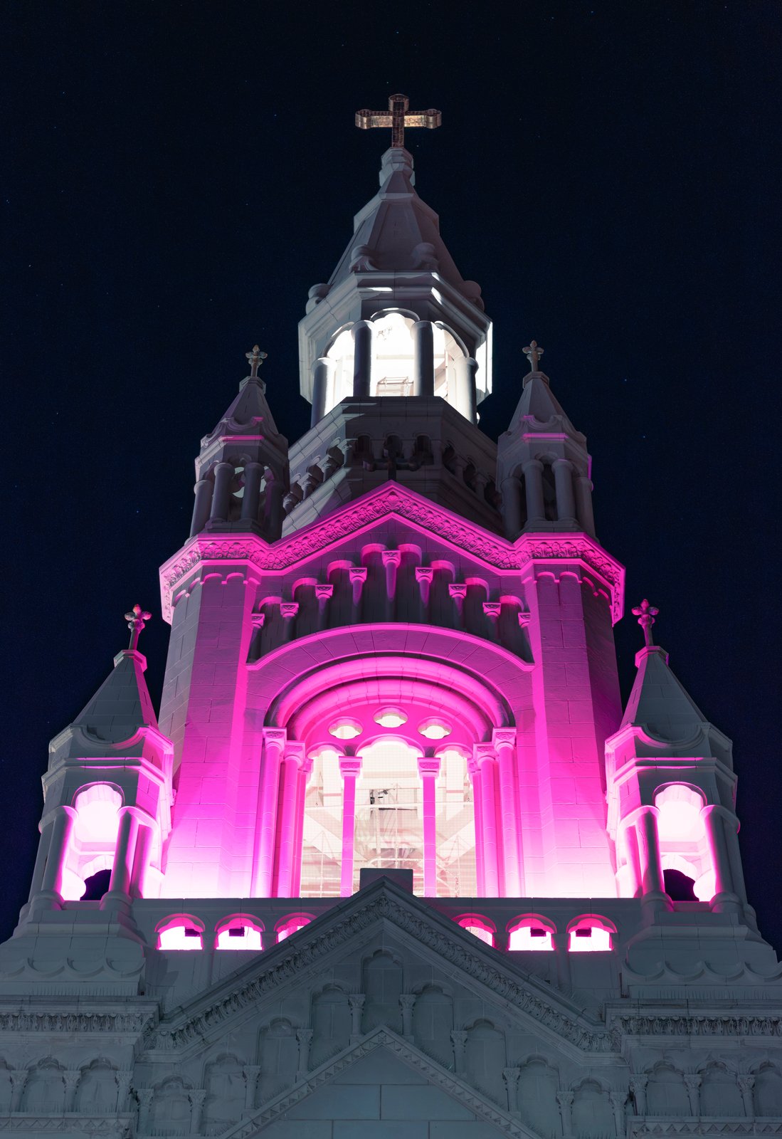 A church tower lit magenta against the night sky