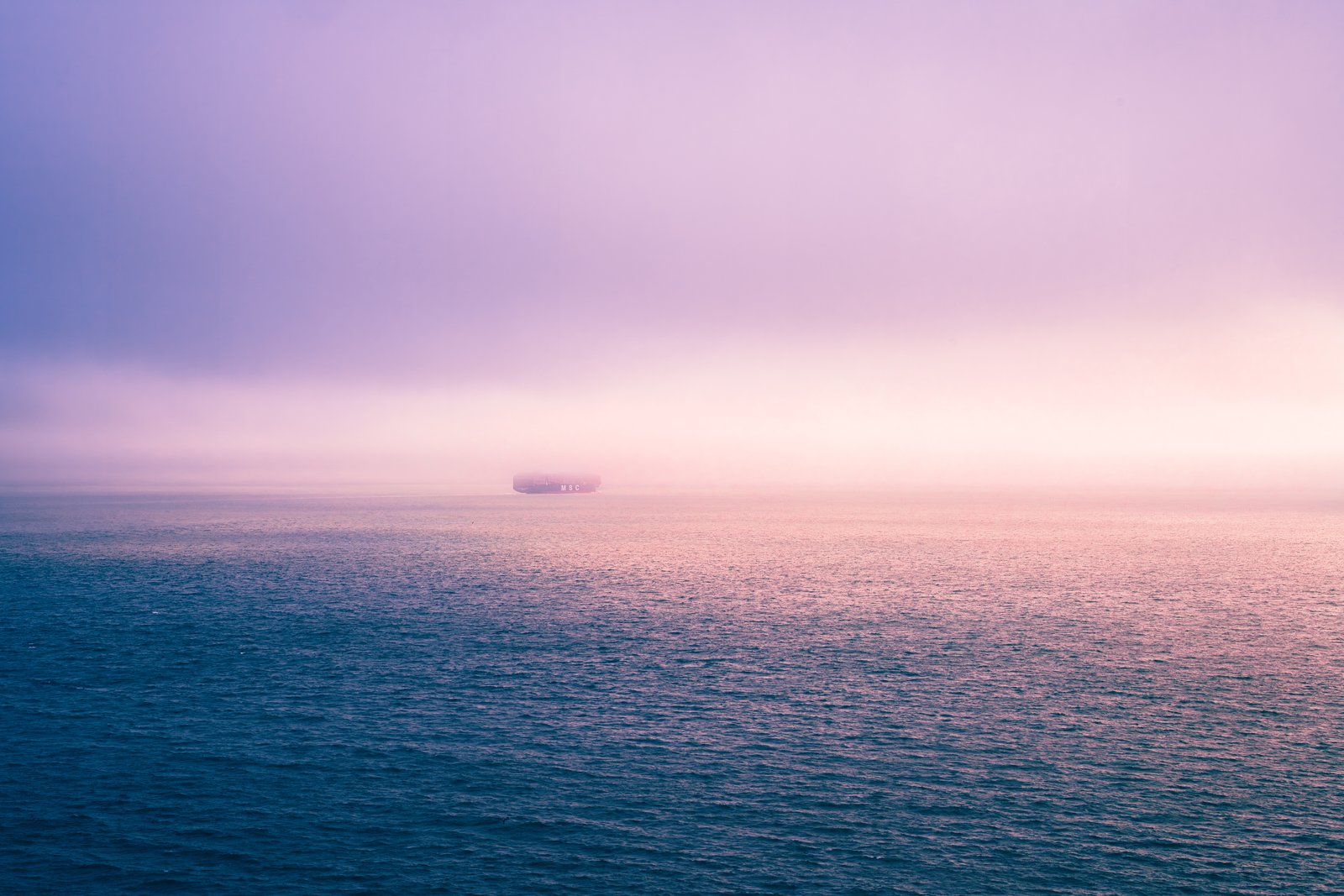 A single ship barely visible in lavender fog at sea