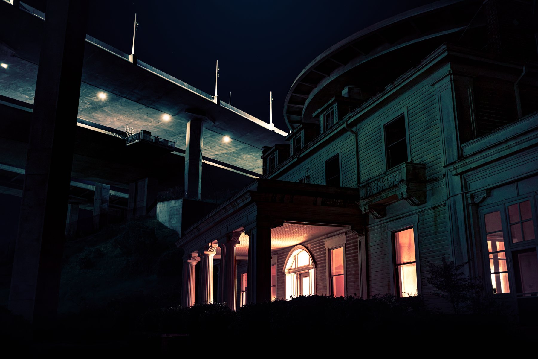 A historic Victorian building lit warmly at night, dwarfed by a freeway overpass above it