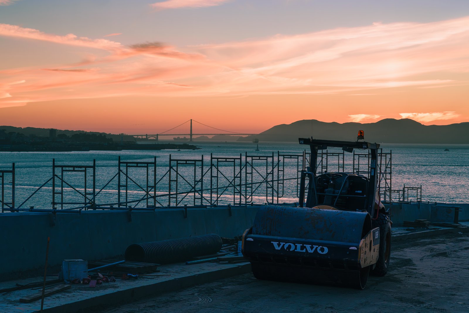 Construction equipment on a pier with the Golden Gate Bridge at sunset behind it