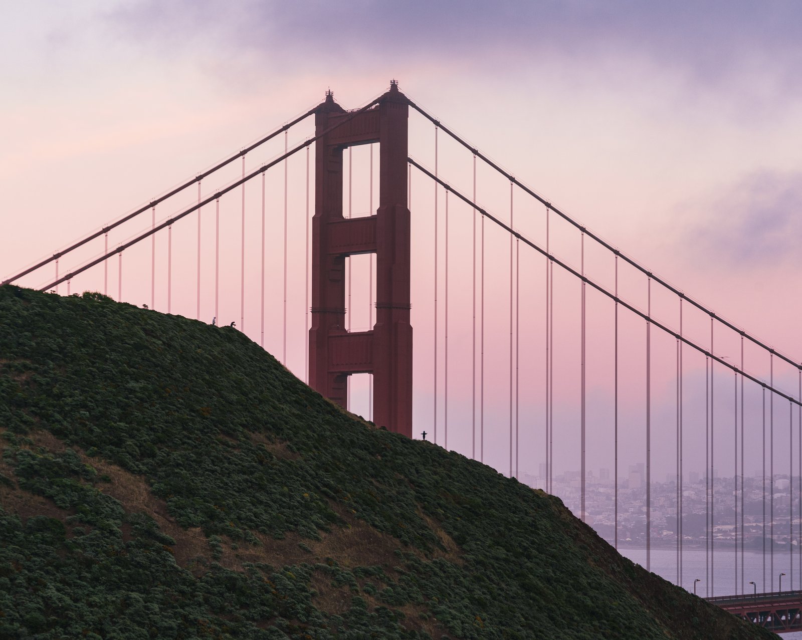 Golden Gate Bridge tower rising over a headlands hill at dusk