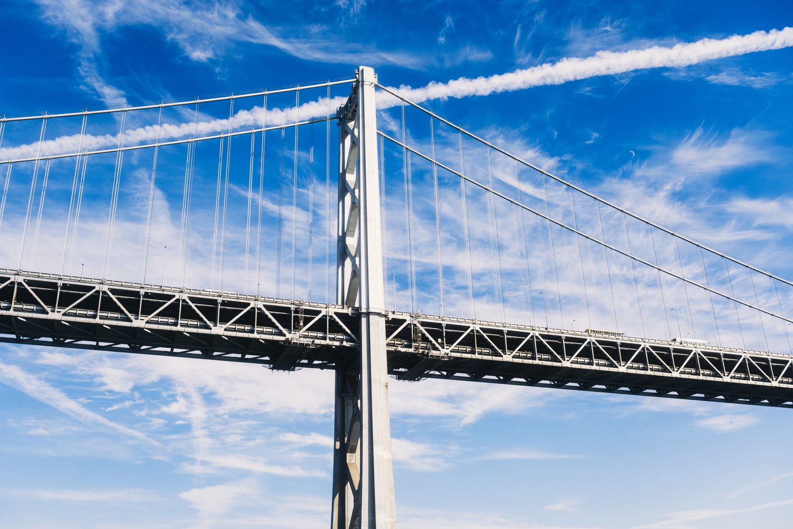 Bay Bridge tower against a blue sky with a contrail