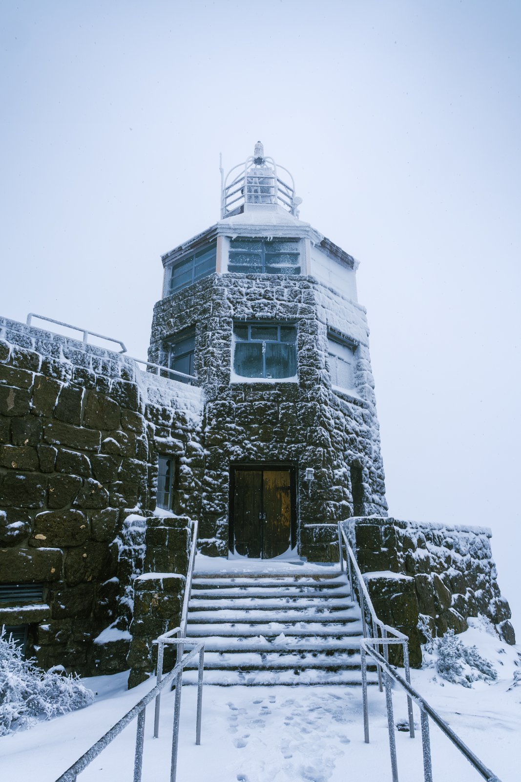 A snow-covered stone tower with a staircase leading up to its door