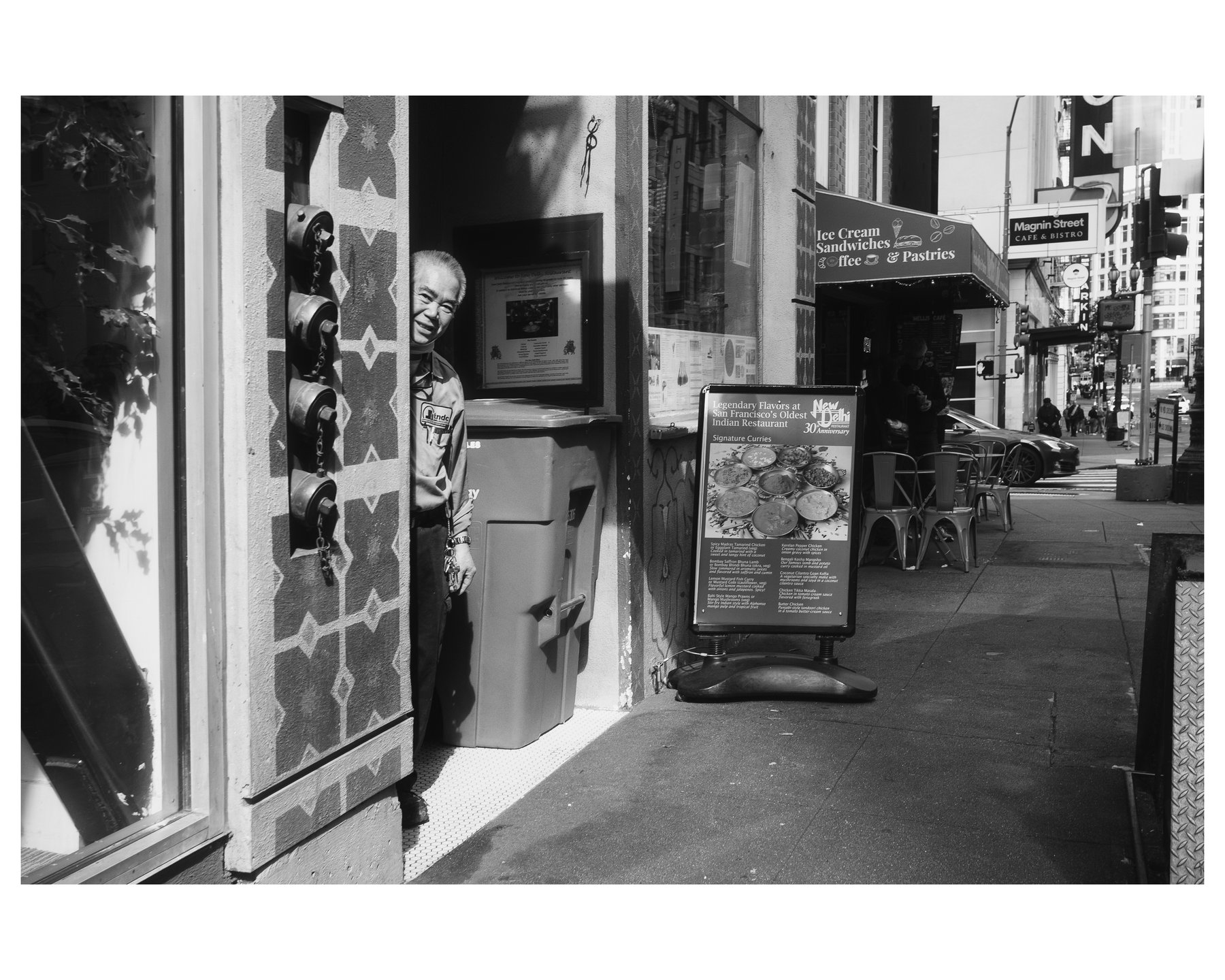 A man in a doorway beside a trash bin, glancing out at the street