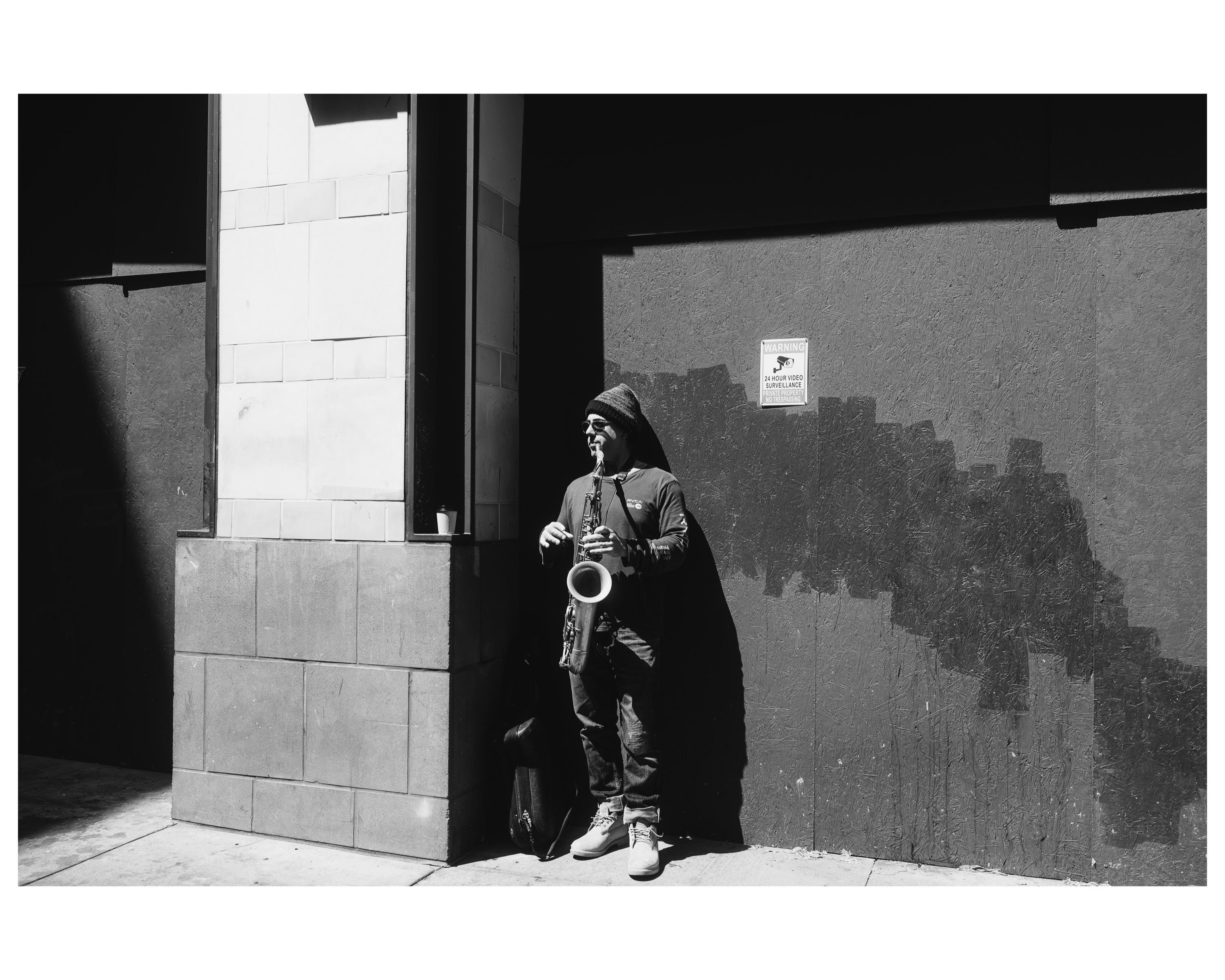 A saxophone player performing in a hard-edged shadow against a plywood wall
