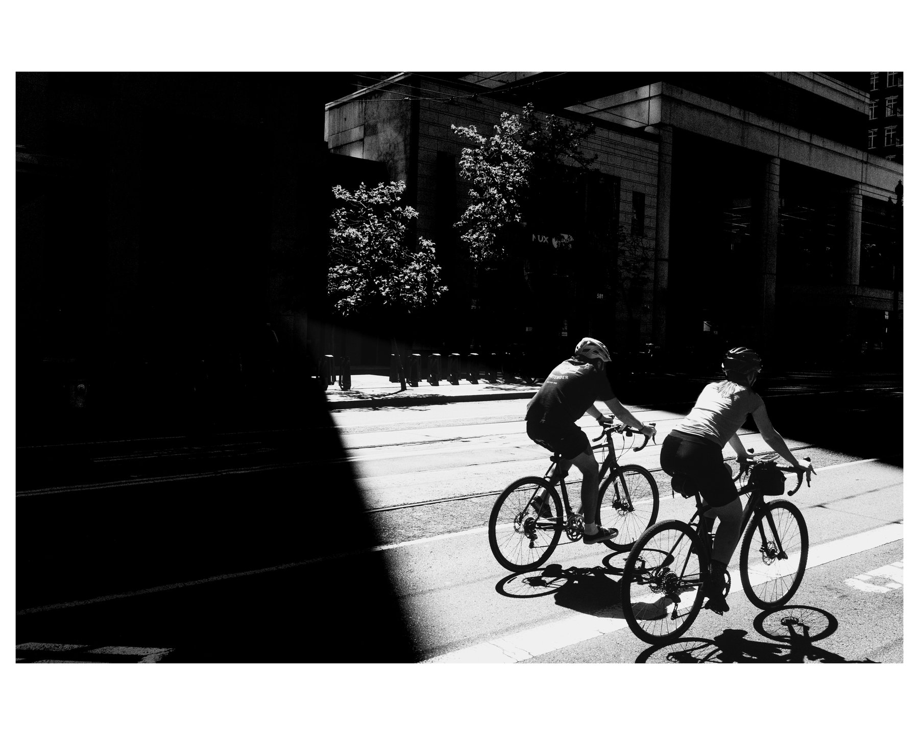 Two cyclists riding out of deep shadow into bright sunlight