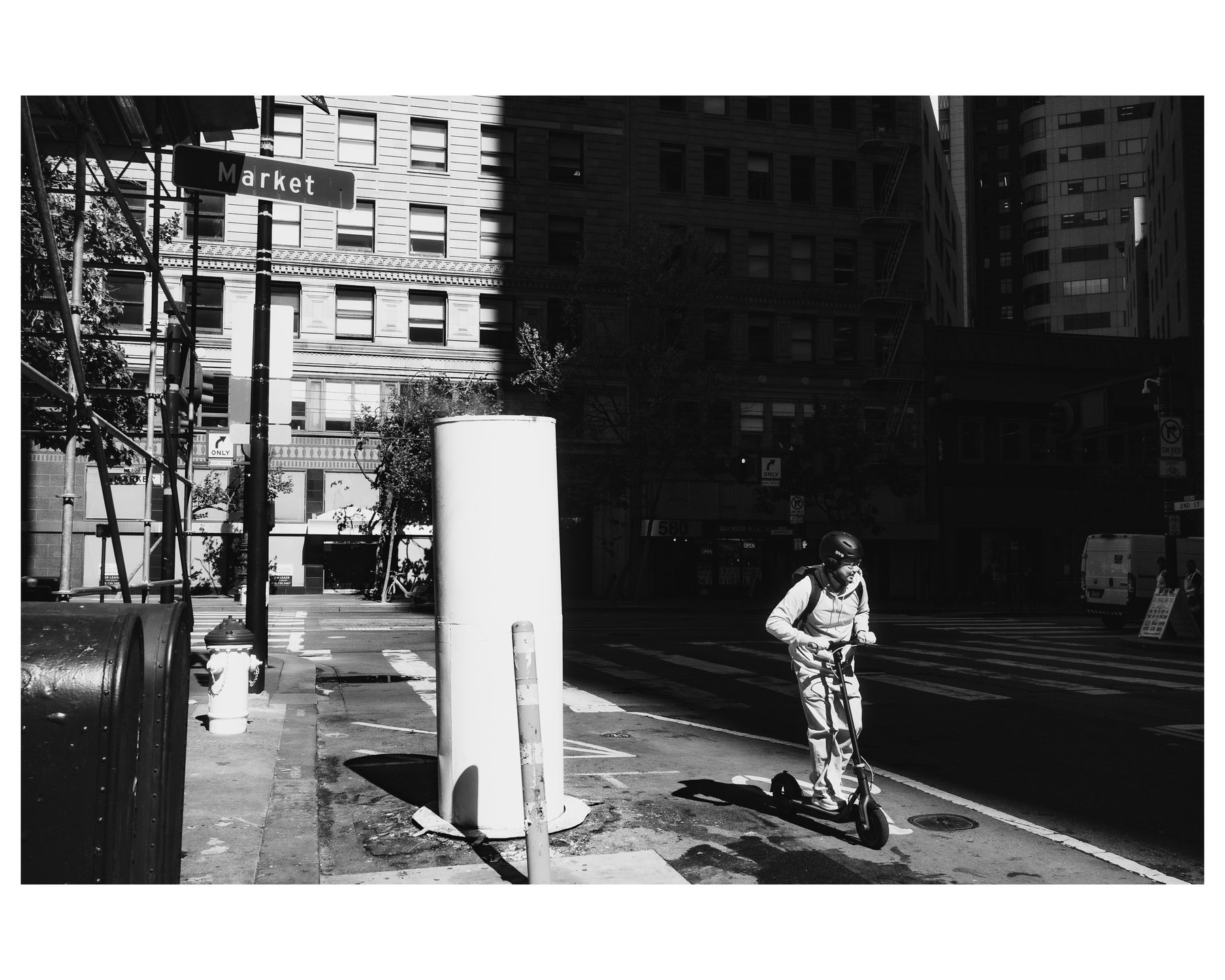 A man riding an electric scooter through a sharp band of light on Market Street