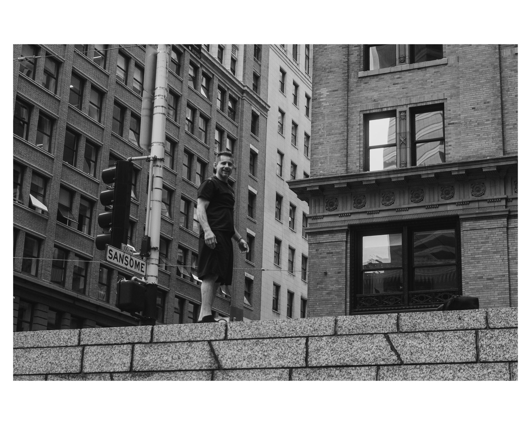 A man smiling while balancing on top of a granite wall on Sansome Street