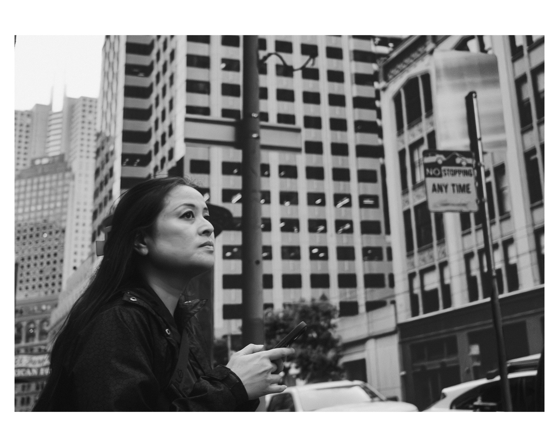 A woman's profile against a backdrop of high-rise buildings, looking up while holding her phone