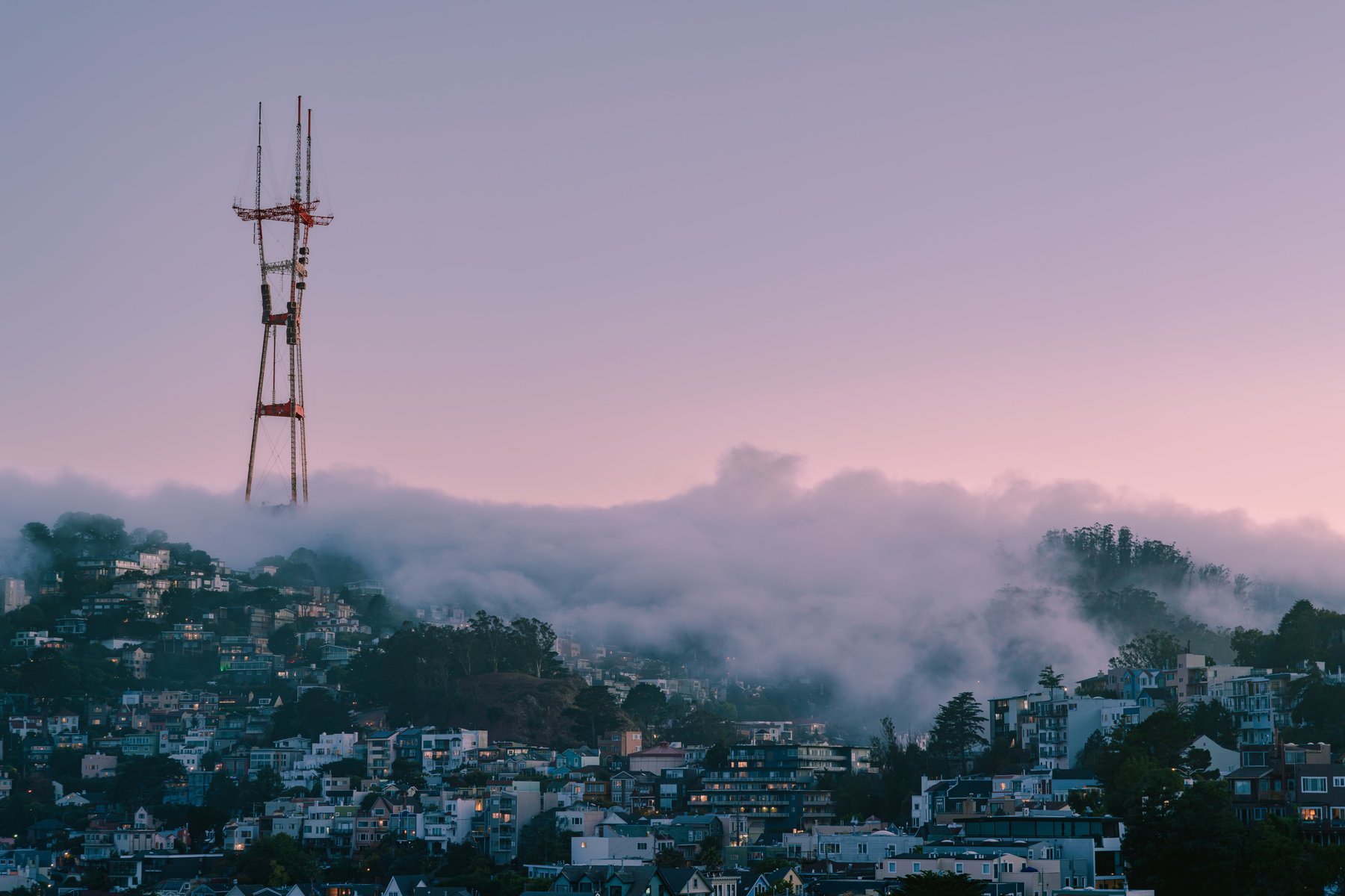 Sutro Tower rising through fog over a San Francisco hillside at dusk