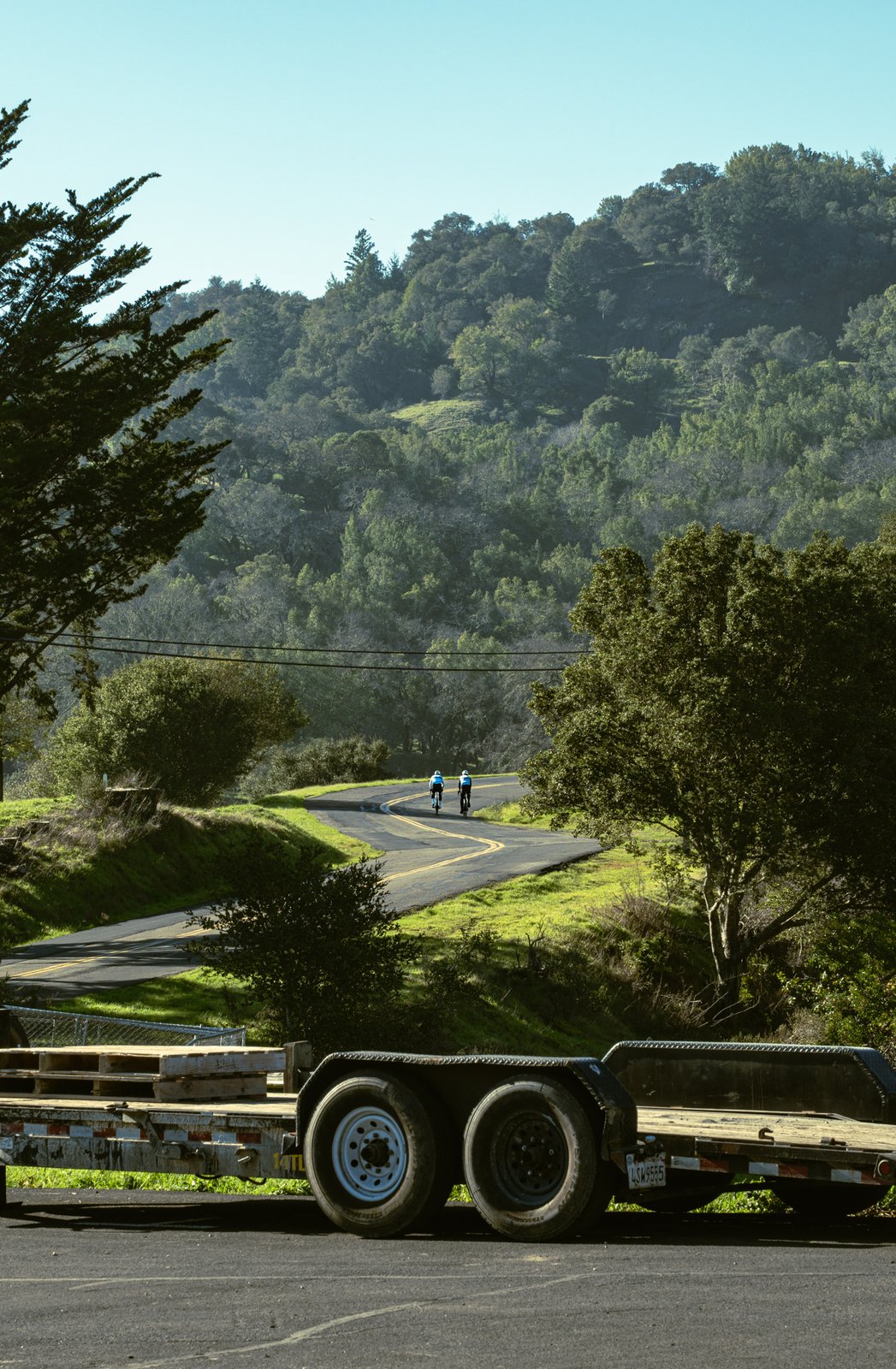 An equipment trailer in the foreground with cyclists on a winding road behind