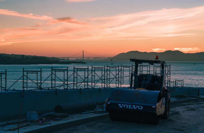 Construction equipment on a pier with the Golden Gate Bridge at sunset behind it
