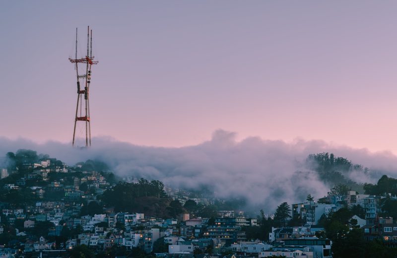 Sutro Tower rising through fog over a San Francisco hillside at dusk