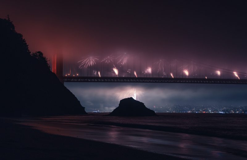 Fireworks bursting through fog beneath the Golden Gate Bridge at night
