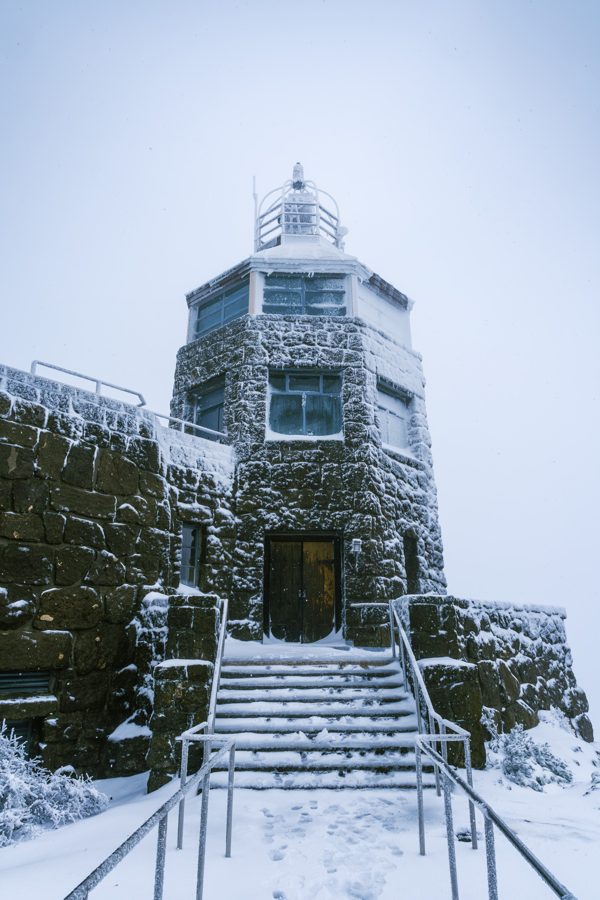A snow-covered stone tower with a staircase leading up to its door